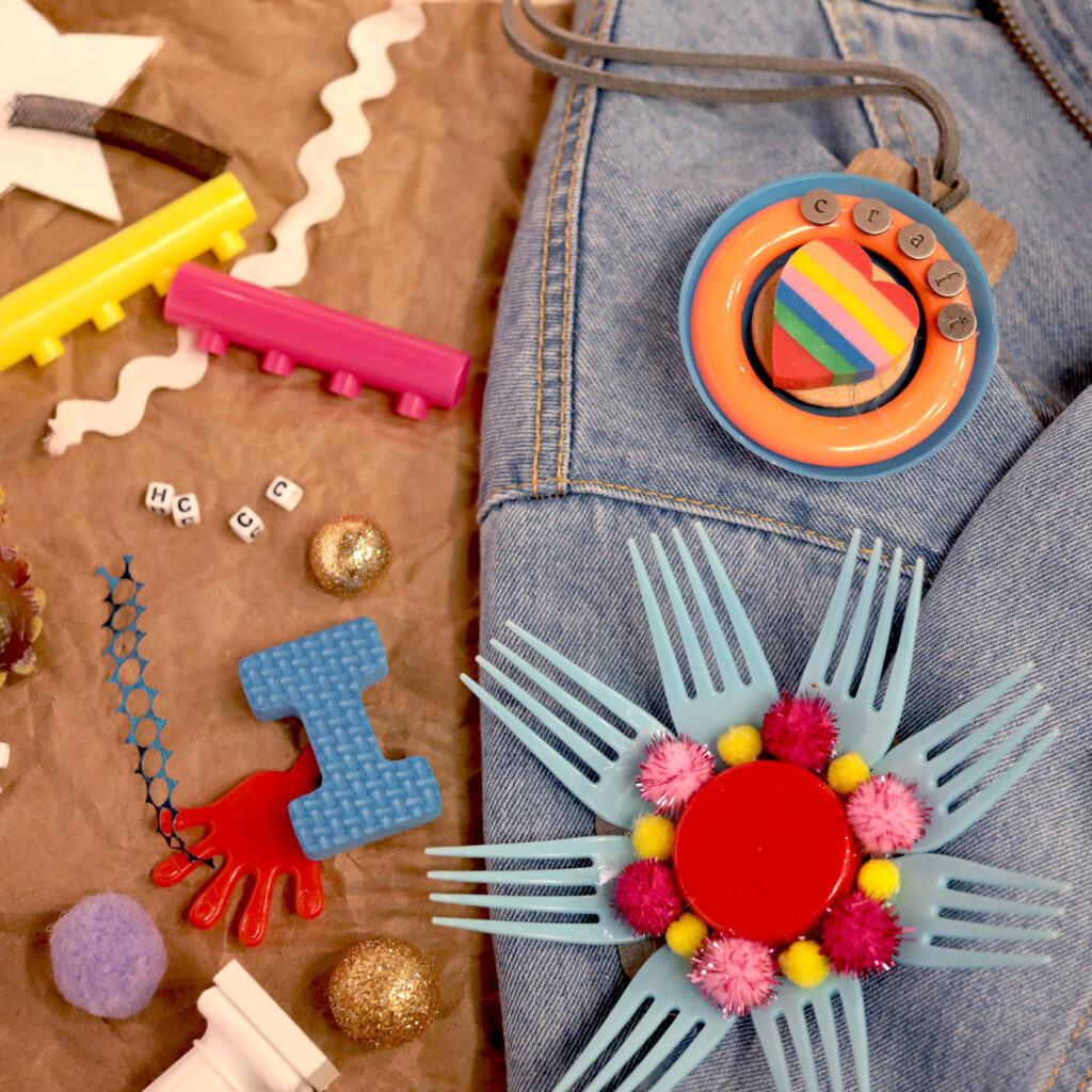 Image of samples of jewelry made from various found objects, laying on a table and on a denim jacket.